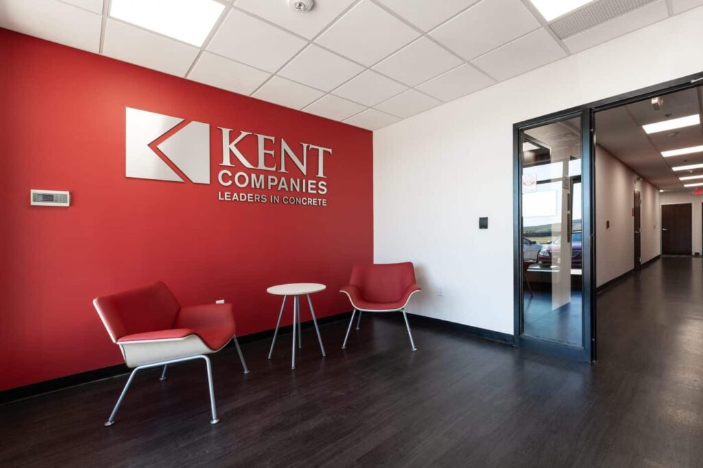 Kent Companies office lobby features a red accent wall, two red chairs, a white table, and signage: Leaders in Concrete.