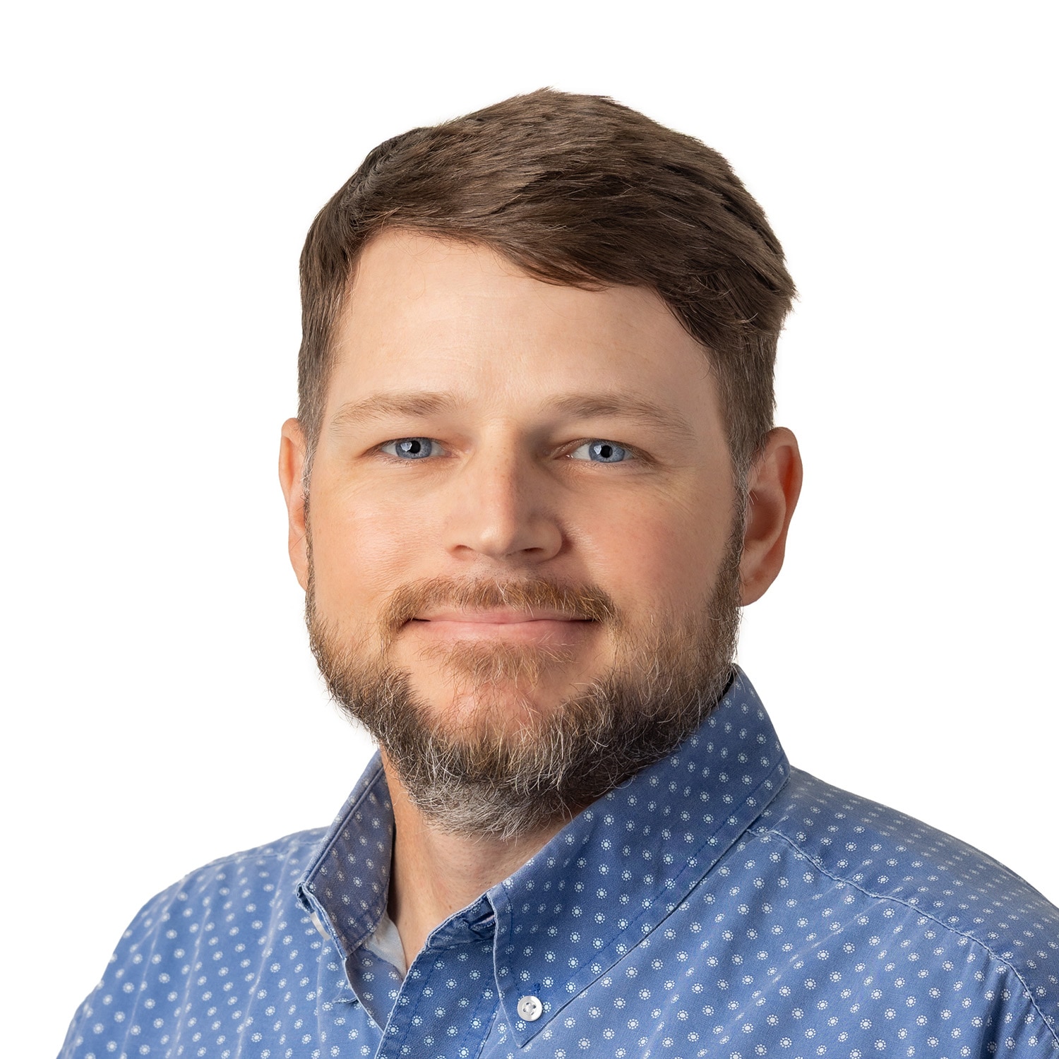 Cody Lightfoot, with short brown hair, a beard, and a blue patterned shirt, smiles in front of a white background.