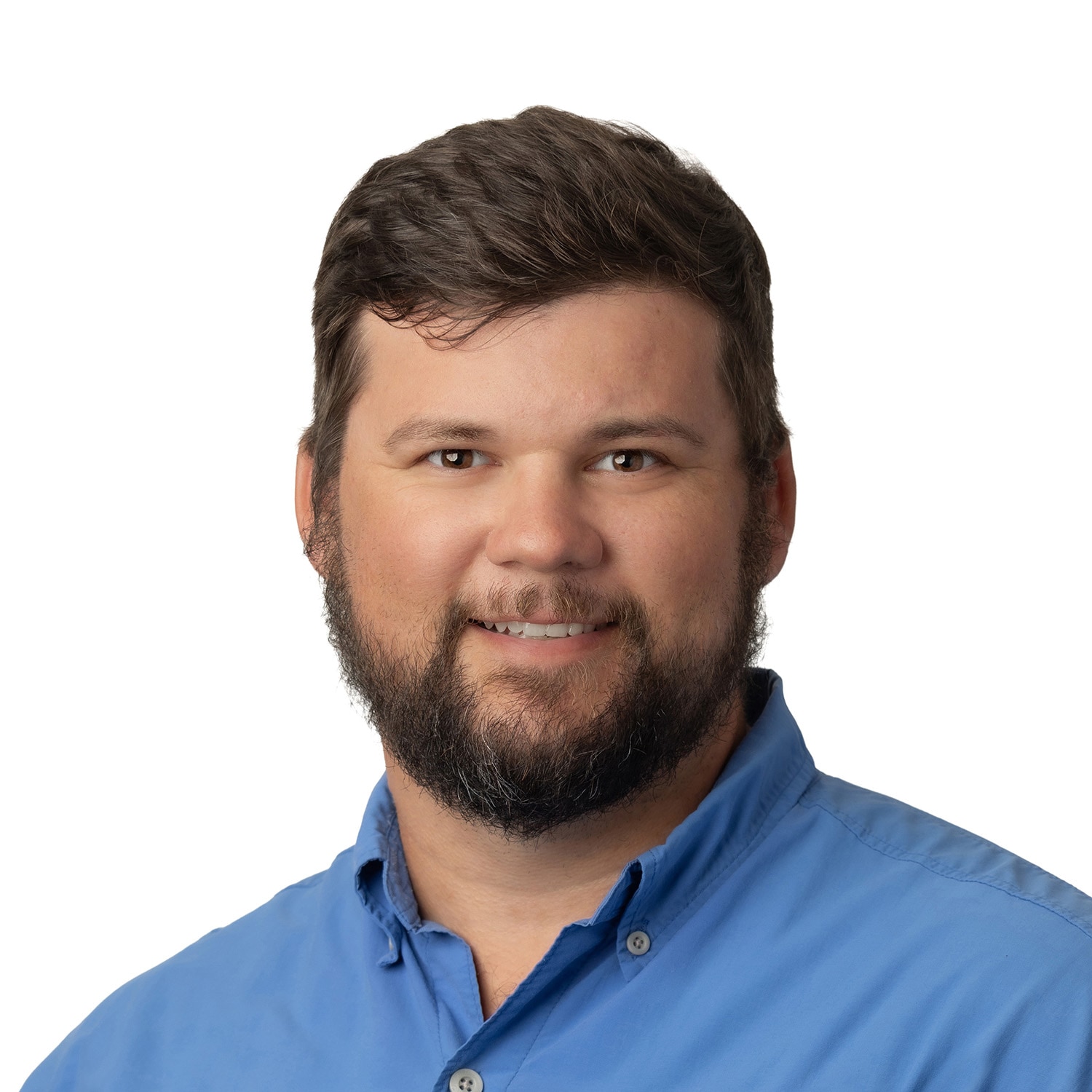 A man with short brown hair and a beard, wearing a blue collared shirt, smiles at the camera against a white background.