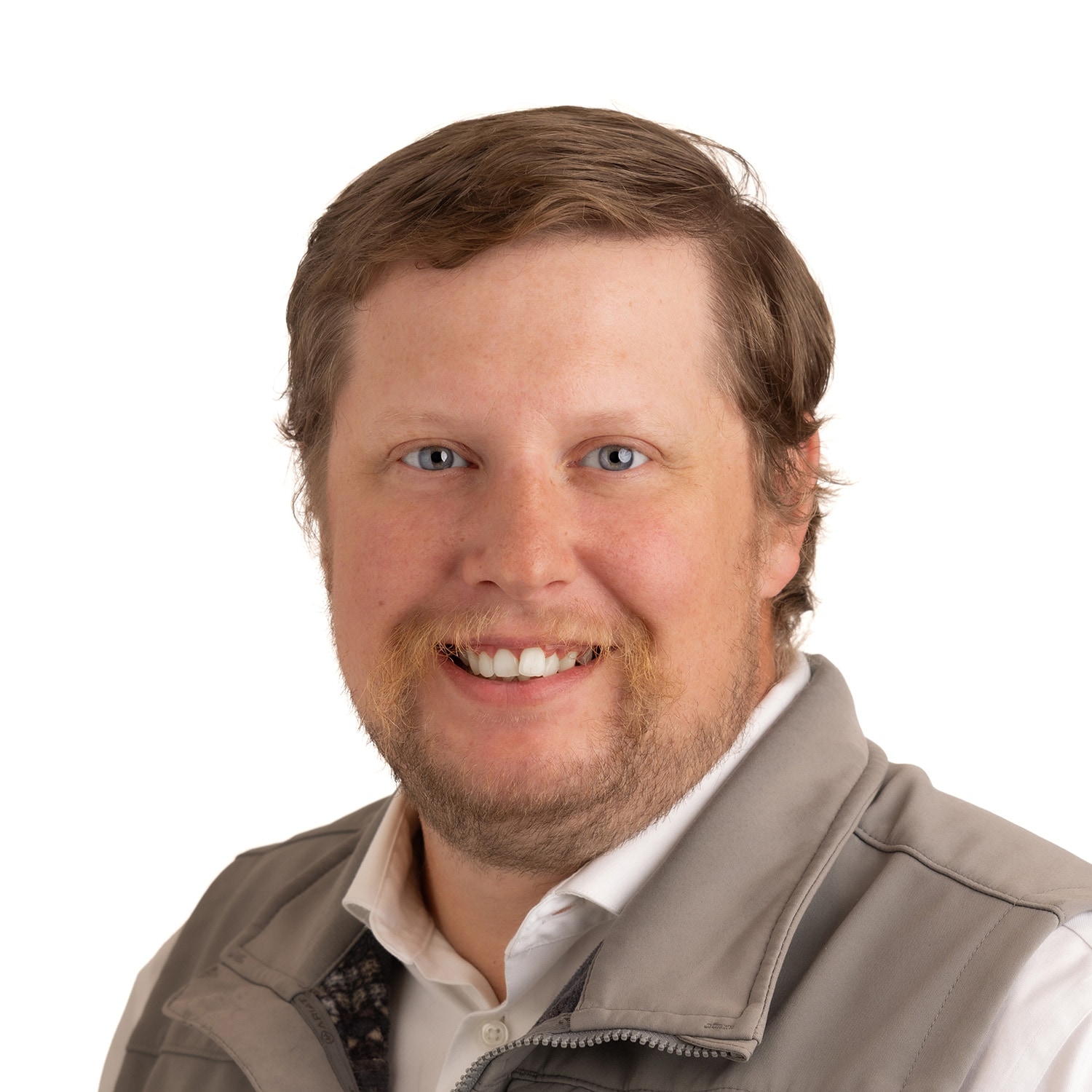 Smiling man with light brown hair and beard, wearing a gray vest over a white shirt, on a white background.