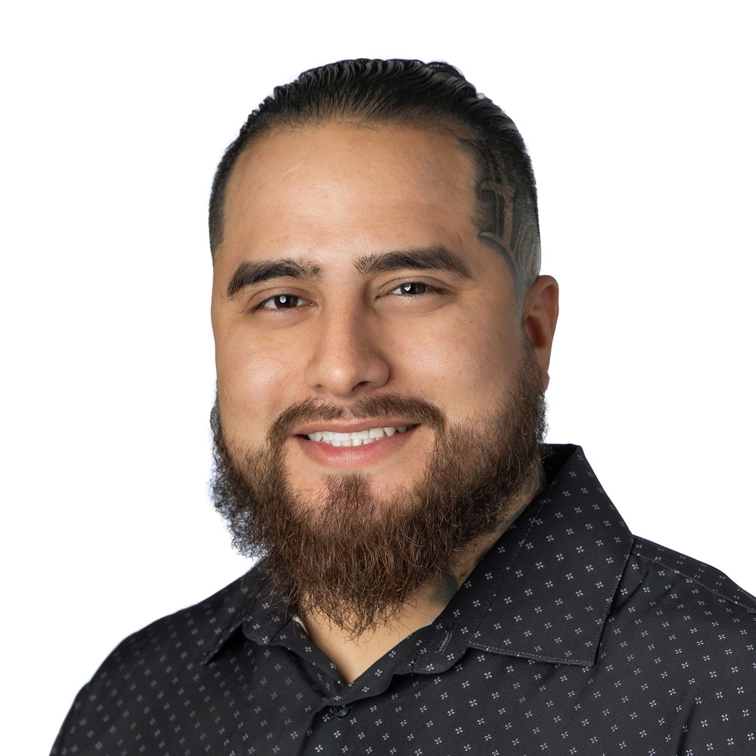 Smiling man with a beard and dark hair wearing a patterned black shirt, pictured on a white background.